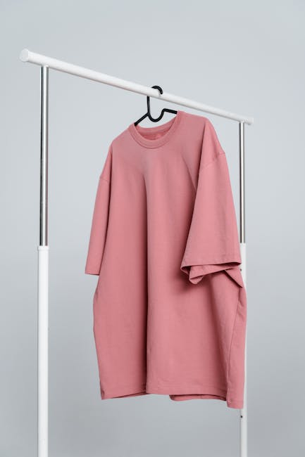 A minimalist pink unisex t-shirt hanging on a white rack against a light background.